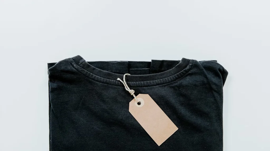 A flat lay image of a folded black t-shirt with a blank, light brown tag on a white background.