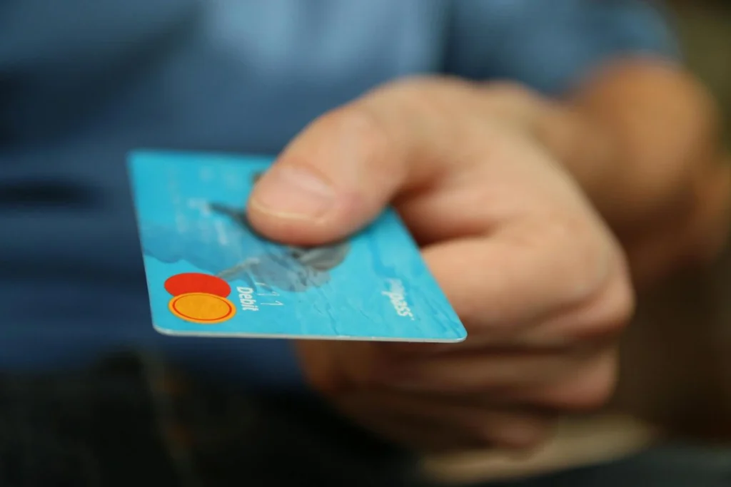 A close-up shot of a hand holding a blue debit card with a red and orange circle logo. The word "Debit" is visible on the card.